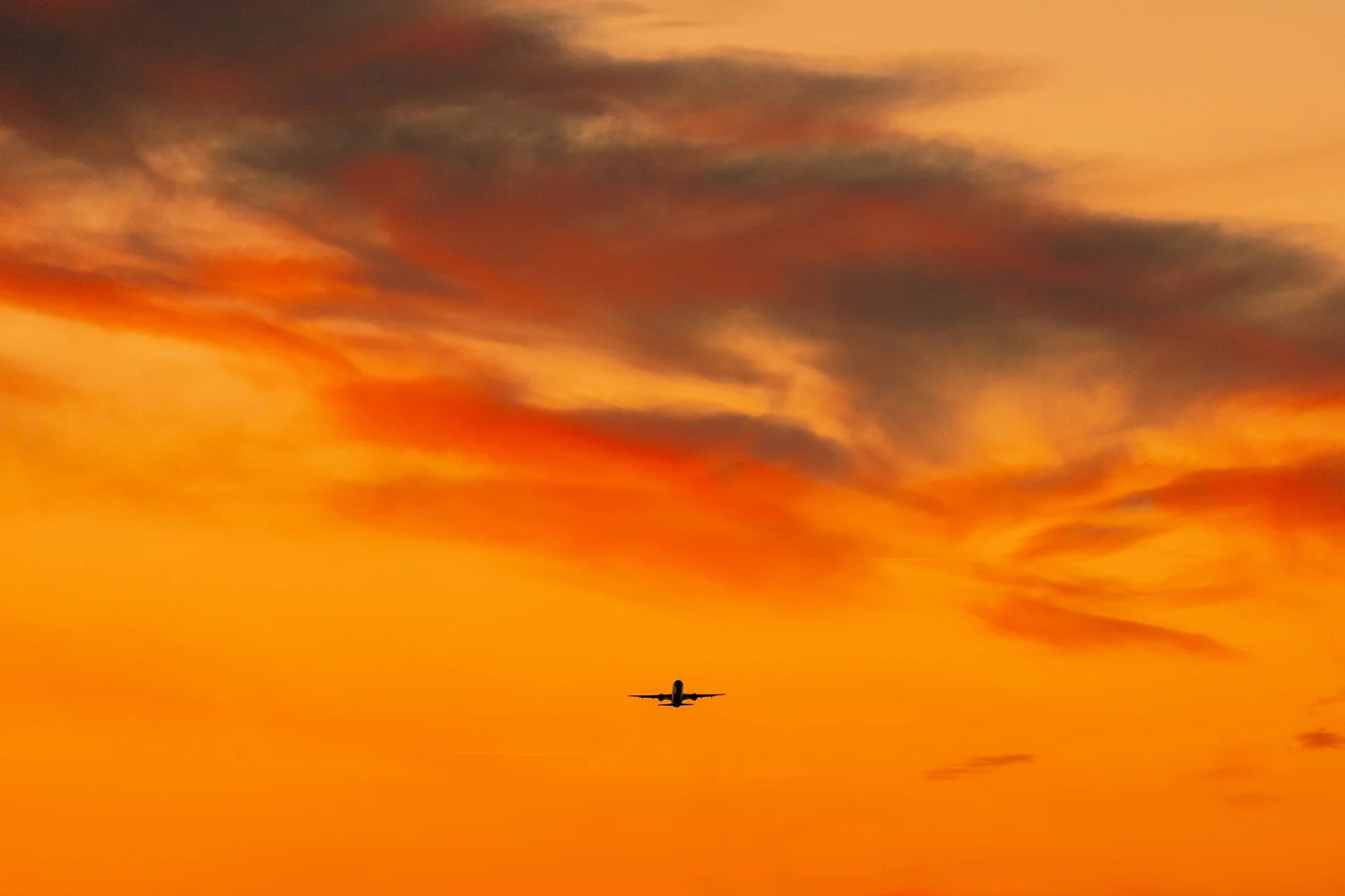 An aeroplane crossing an orange sunset sky