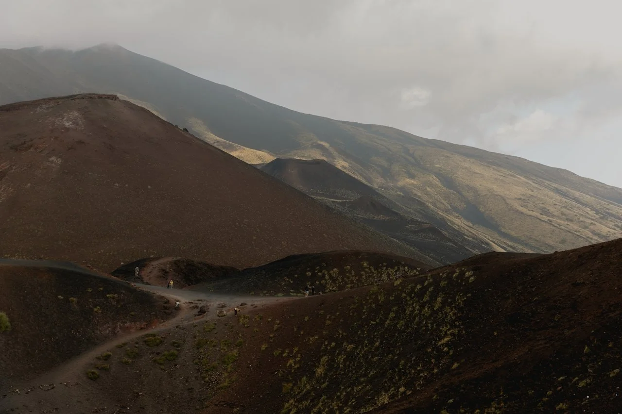 Walkers crossing a dark volcanic landscape under a pale sky