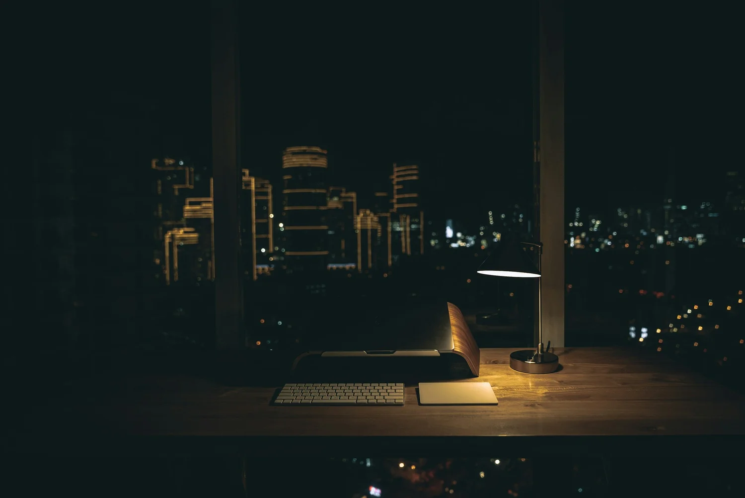 A laptop open on a desk by a window at night, city lights beyond