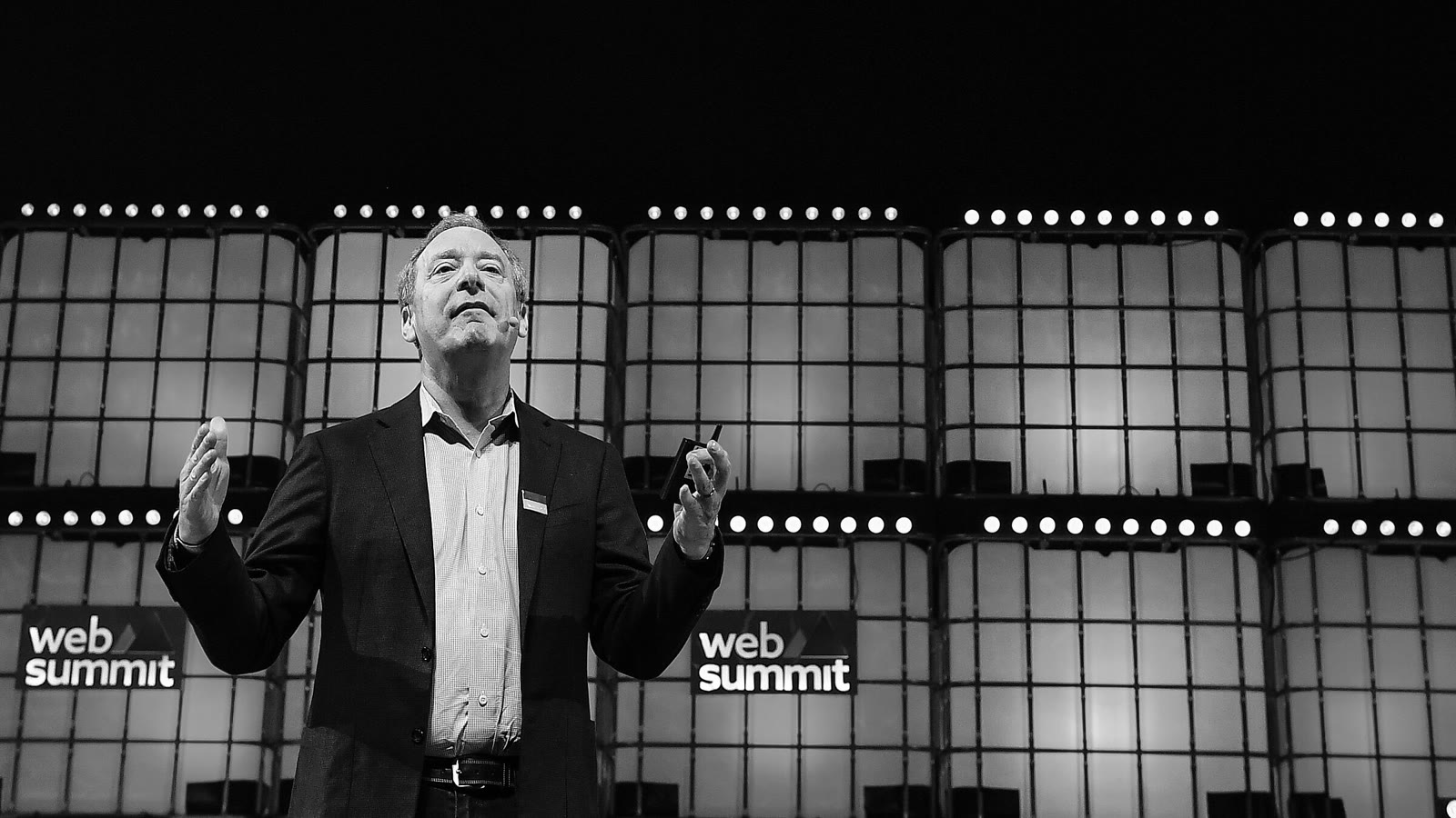 A speaker addresses a packed arena from a vast conference stage